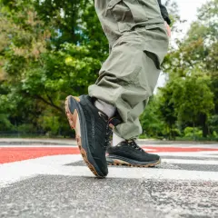 Osoba w spodniach cargo stawia kroki na pasach w czarnych butach Merrell Moab Speed 2 z brązową podeszwą.