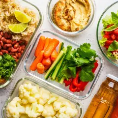 Gotowe jedzenie na biwak: ryż z fasolą i pieczarkami, warzywa pokrojone w słupki, kalafior, sałatka z pomidorów i awokado, hummus, soki.
