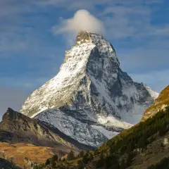 Majestatyczne szwajcaria góry, ośnieżony szczyt Matterhorn z chmurką na wierzchołku, otoczony jesiennymi zboczami i lasem.