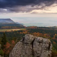 Widok z kamiennego urwiska na jesienny krajobraz Gór Stołowych. Szczeliniec Wielki w jesiennej szacie, z lasami mieniącymi się kolorami.