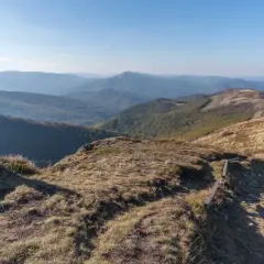 Kobieta odpoczywa na szczycie, podziwiając rozległe, **tajemnicze miejsca w Bieszczadach**. W tle widać kolejne pasma górskie.