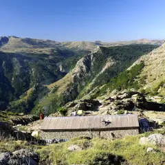 Kamienny schron na GR20 Korsyka, otoczony skalistymi zboczami i zielonymi dolinami.