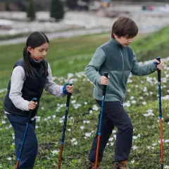 Dzieci z kijkami trekkingowymi idą przez kwitnącą łąkę. W tle widać resztki śniegu, co sugeruje wczesną wiosnę w Tatrach zimą z dzieckiem.