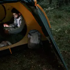 Mężczyzna pracuje na laptopie w namiocie, otoczony lasem. Plecak stoi obok, gotowy do dalszej podróży pod namiot.