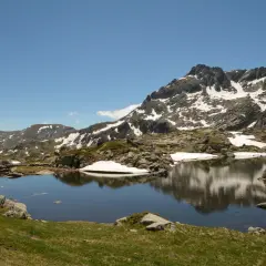 Góry Pirin z jeziorem odbijającym skaliste szczyty i resztki śniegu.