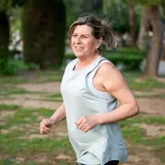 Uśmiechnięta kobieta w średnim wieku cieszy się bieganiem 5 km dziennie w parku.