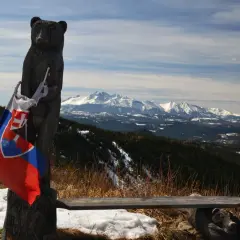 Drewniany niedźwiedź z flagą Słowacji na szczycie Veterny Vrch, z widokiem na ośnieżone Tatry.