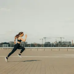 Kobieta w stroju sportowym biegnie po betonowym placu. To inspiracja dla każdego, kto szuka poradnika biegacza.