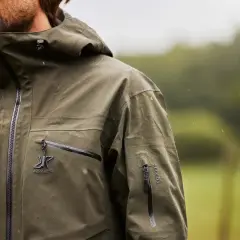 Mężczyzna w zielonej kurtce z kapturem, na której widać krople deszczu. Taka kurtka water repellent co to znaczy? To ochrona przed wilgocią.