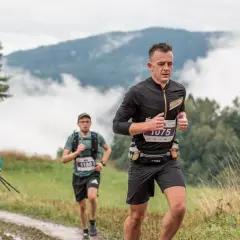 Uczestnicy festiwalu biegowego Piwniczna pokonują górski szlak. W tle mgliste pasma górskie.