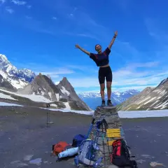 Szczęśliwa turystka na szczycie kamiennego kopca, z plecakami i kijkami trekkingowymi u stóp, na tle majestatycznych Alp podczas ultra-trail du mont-blanc.