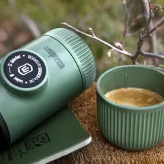 Zielona kawa w górach. Nanopresso i filiżanka świeżego espresso na drewnianym pniu, wśród gałązek. Idealny poranek w naturze.