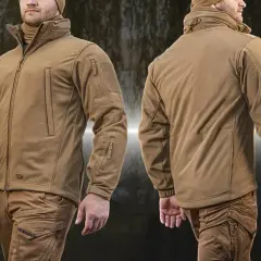 Mężczyzna w beżowej kurtce taktycznej z materiału softshell. Kurtka ma liczne kieszenie i ściągacze.