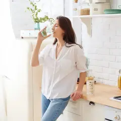 Kobieta pije wodę, która jest świetnym wyborem, co pić na zakwasy. Woda nawadnia i pomaga w regeneracji.