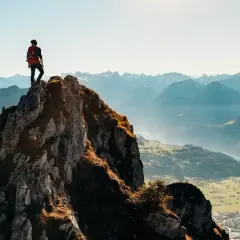 Wspinacz na szczycie skalistego wzniesienia, podziwia letnie krajobrazy Alp.