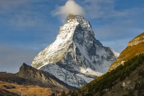 Majestatyczne szwajcaria góry, ośnieżony szczyt Matterhorn z chmurką na wierzchołku, otoczony jesiennymi zboczami i lasem.
