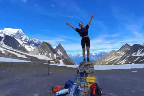 Szczęśliwa turystka na szczycie kamiennego kopca, z plecakami i kijkami trekkingowymi u stóp, na tle majestatycznych Alp podczas ultra-trail du mont-blanc.