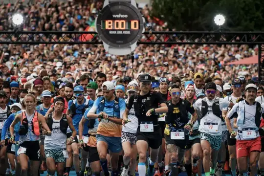 Tłum biegaczy na starcie ultra maratonu. Zegarek na nadgarstku pokazuje 18:00:10.