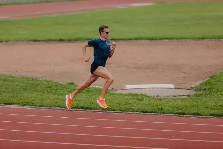 Mężczyzna w okularach i sportowym stroju wykonuje trening biegowy na 3 km po bieżni stadionu.
