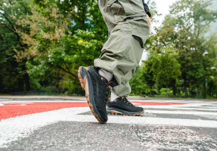 Osoba w spodniach cargo stawia kroki na pasach w czarnych butach Merrell Moab Speed 2 z brązową podeszwą.