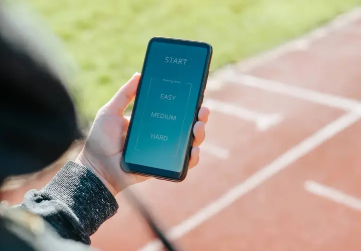 Dłoń trzyma smartfon z ekranem aplikacji do biegania. Wybierz poziom treningu: łatwy, średni lub trudny. To najlepsza aplikacja do biegania!