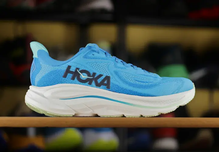 Niebieskie buty sportowe Hoka z charakterystycznym logo. To firma znana z innowacyjnych rozwiązań w obuwiu biegowym.