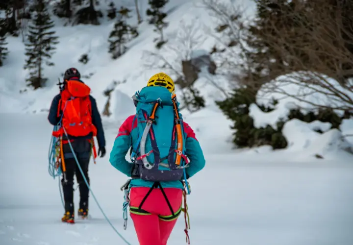 Dwóch alpinistów w zimowym krajobrazie, z plecakami i sprzętem. To ich lista rzeczy na wyjazd w góry zimą.