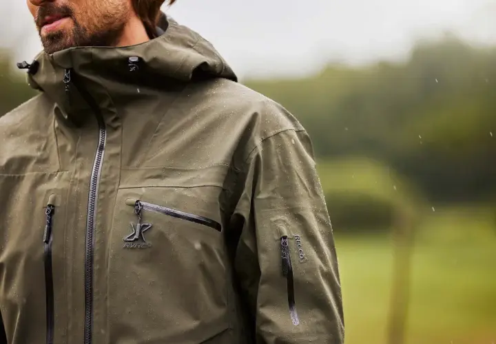 Mężczyzna w zielonej kurtce z kapturem, na której widać krople deszczu. Taka kurtka water repellent co to znaczy? To ochrona przed wilgocią.