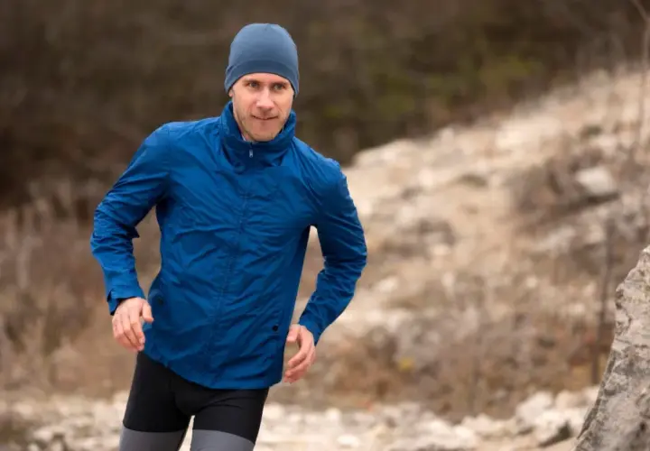Mężczyzna w niebieskiej kurtce softshell i czapce biegnie po kamienistym terenie. Pamiętaj, jak prać softshell, by służył Ci latami.