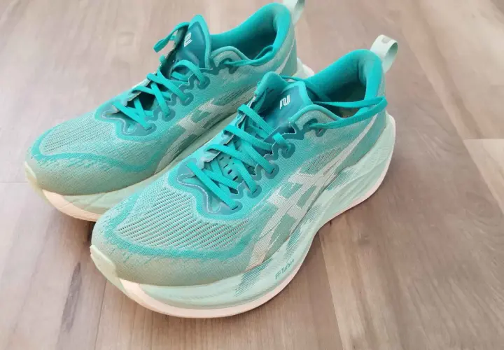 Turkusowe buty do biegania z białym logo, model superblast 2, leżą na drewnianej podłodze.