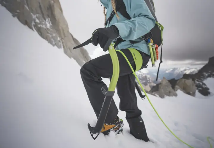 Alpinista używa czekana do wspinaczki po ośnieżonym zboczu. To narzędzie, co to jest czekan, pomaga w utrzymaniu równowagi i pokonywaniu trudnego terenu.