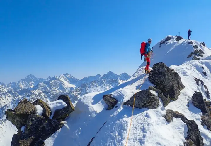 Wspinaczka zimą na Orlą Perć. Dwóch alpinistów na ośnieżonym szczycie, jeden z nich asekurowany liną.