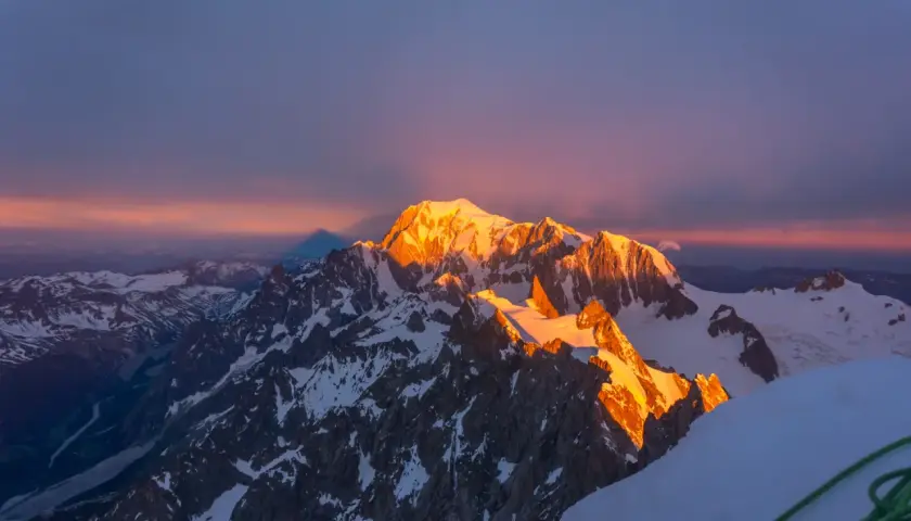 Złote światło wschodu słońca oświetla szczyt Mont Blanc, rzucając długi cień na ośnieżone góry.