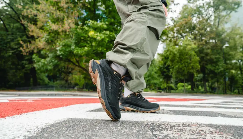 Osoba w spodniach cargo stawia kroki na pasach w czarnych butach Merrell Moab Speed 2 z brązową podeszwą.