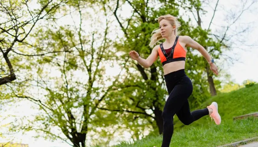 Młoda kobieta w sportowym stroju biegnie po ścieżce w parku. To świetny przykład na bieganie dla początkujących, pełne energii i radości.