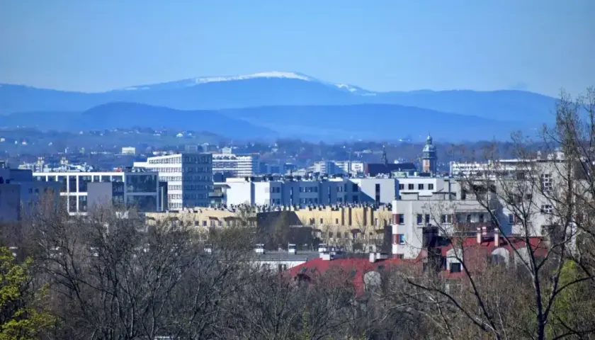 Widok na nowoczesne budynki Krakowa z oddali, na horyzoncie majaczy ośnieżona Babia Góra z Krakowa.