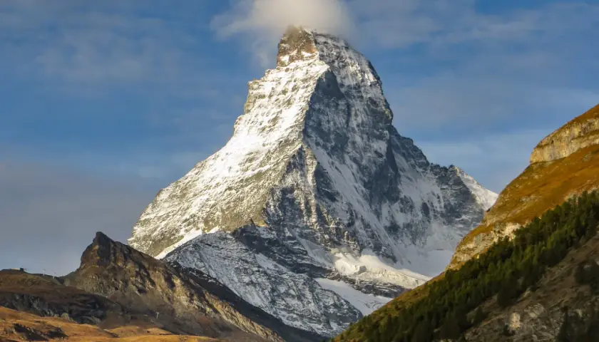 Majestatyczne szwajcaria góry, ośnieżony szczyt Matterhorn z chmurką na wierzchołku, otoczony jesiennymi zboczami i lasem.