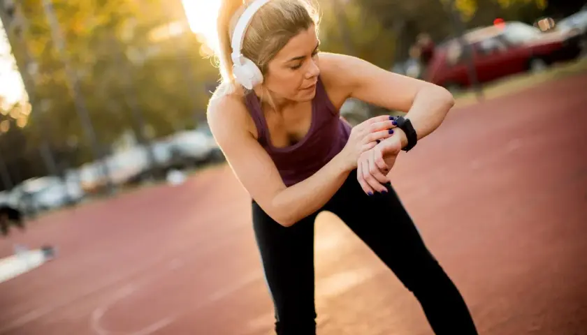 Kobieta w słuchawkach sprawdza czas na zegarku sportowym, przygotowując się do biegu na 2 km.