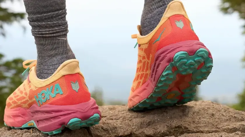 Kolorowe buty Hoka na kamienistym szlaku. Firma Hoka słynie z amortyzacji i innowacyjnych rozwiązań dla biegaczy.