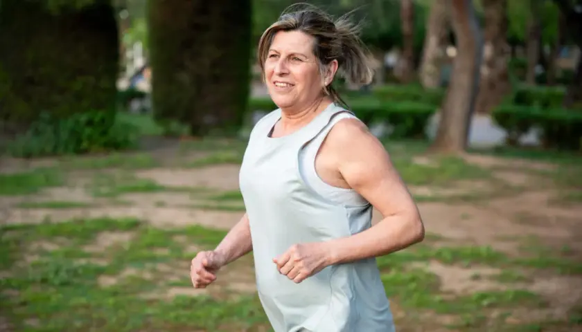 Uśmiechnięta kobieta w średnim wieku cieszy się bieganiem 5 km dziennie w parku.