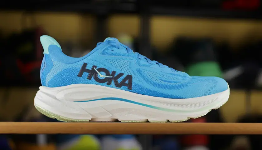 Niebieskie buty sportowe Hoka z charakterystycznym logo. To firma znana z innowacyjnych rozwiązań w obuwiu biegowym.