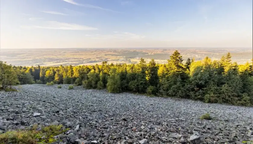 Kamieniste zbocze schodzi ku lasowi, a za nim rozciąga się krajobraz pól i łąk. Widok z łysicy zapiera dech.