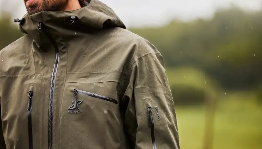 Mężczyzna w zielonej kurtce z kapturem, na której widać krople deszczu. Taka kurtka water repellent co to znaczy? To ochrona przed wilgocią.