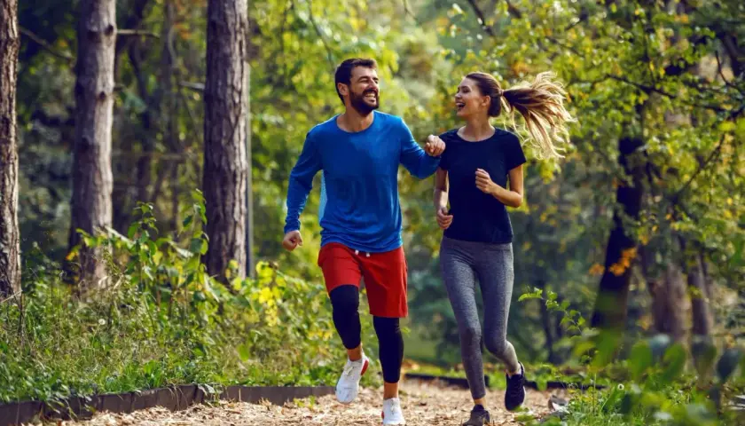 Szczęśliwa para cieszy się wspólnym trail run w jesiennym lesie.
