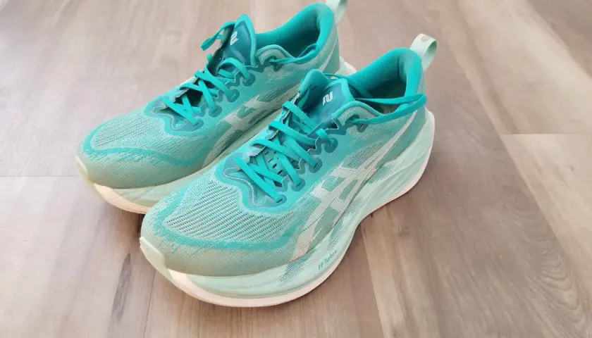 Turkusowe buty do biegania z białym logo, model superblast 2, leżą na drewnianej podłodze.