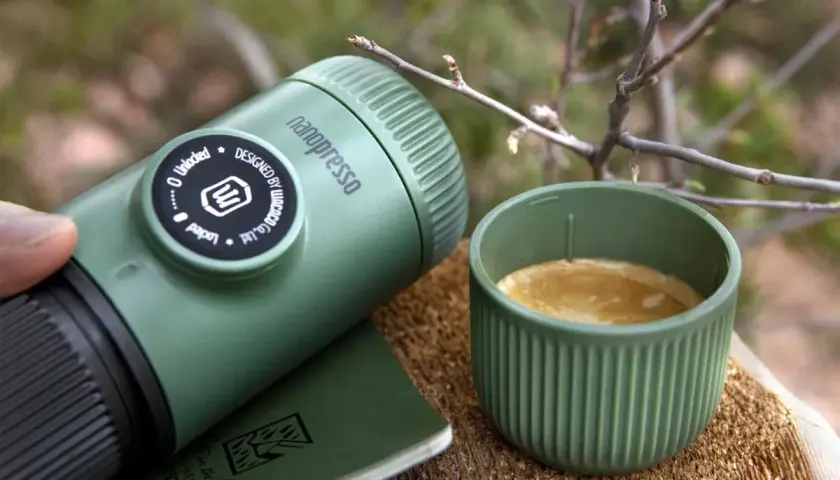 Zielona kawa w górach. Nanopresso i filiżanka świeżego espresso na drewnianym pniu, wśród gałązek. Idealny poranek w naturze.