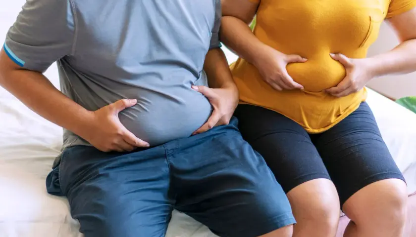 Osoby z nadwagą trzymają się za brzuchy. Zastanawiają się, czy bieżnia odchudza brzuch.
