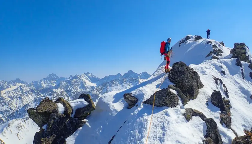 Wspinaczka zimą na Orlą Perć. Dwóch alpinistów na ośnieżonym szczycie, jeden z nich asekurowany liną.