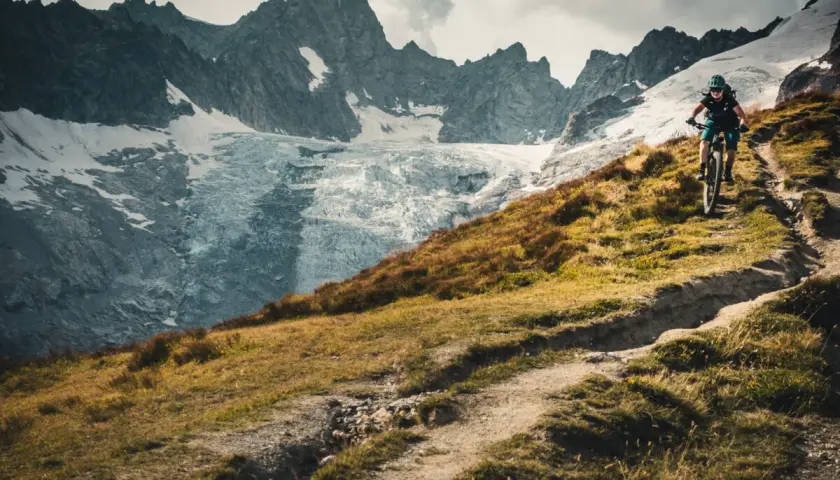 Rowerzysta na szlaku podczas Tour du Mont Blanc, z lodowcem i skalistymi szczytami w tle.
