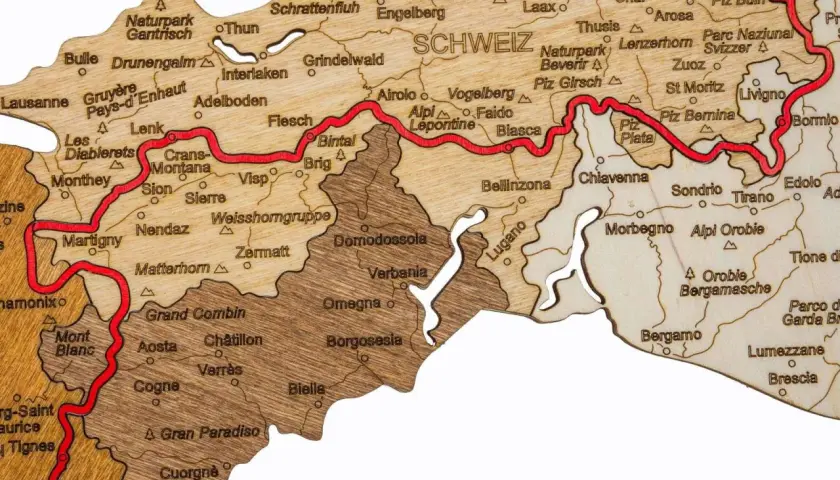 Drewniana mapa Alp z zaznaczoną trasą Via Alpina, pokazująca szczyty i miejscowości takie jak Matterhorn, Zermatt, Lugano i St. Moritz.